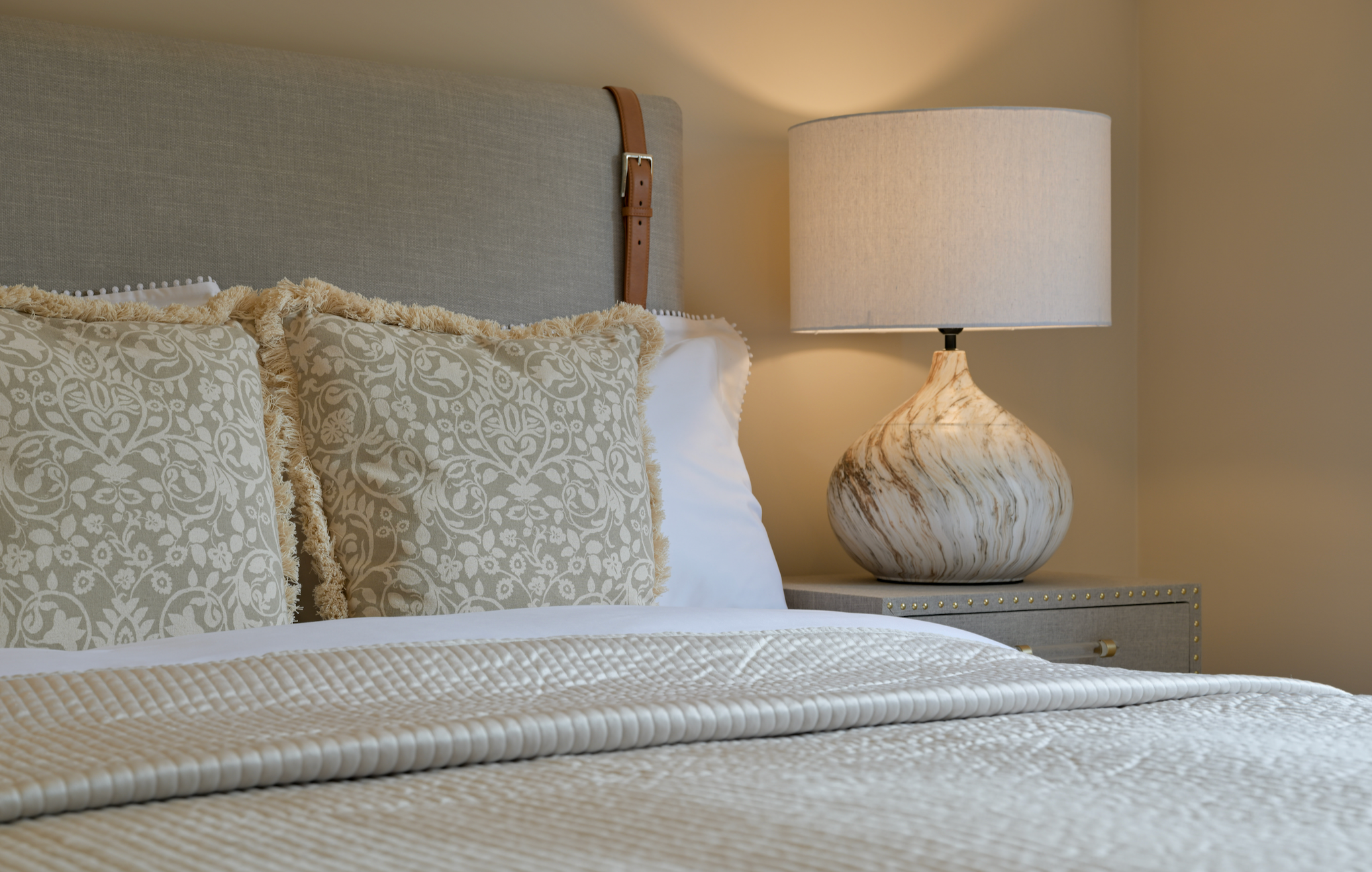 Neatly made bed with patterned pillows and a lamp on a nightstand in a bedroom setting.